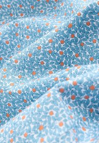 Ljusblått tyg med ett lövmönster i olika nyanser av blått, prytt med små orangea cirklar. Mjuk textur, flödande fall.