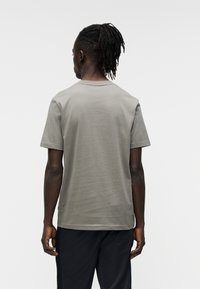 Γκρι κοντ ομάνικη μπλούζα κατασκευασμένη από λείο ύφασμα, με κλασικό στρογγυλό λαιμό και άνετη εφαρμογή, εμφανίζεται από πίσω.