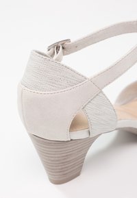 Sandale en daim beige avec des brides en tissu texturé, fermeture à boucle, et talon bloc en bois empilé, vue de côté arrière.