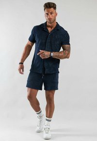 Marinskjorta med knappar och matchande shorts i mjuk tyg. Bärs med vita sneakers och randiga strumpor. Enkel design utan synliga mönster.