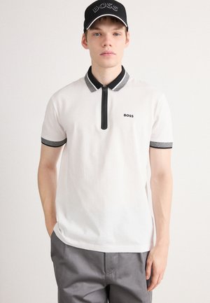 White polo shirt with a black zipper and collar, featuring grey accent details. Worn with grey trousers and a black cap displaying "BOSS."