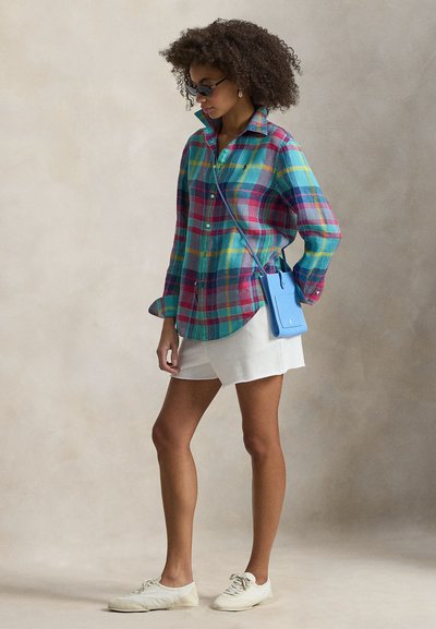 Πολύχρωμο πουκάμισο καρό σε τιρκουάζ, ροζ και κίτρινο, κουμπωμένο, με γιακά. Συνδυασμένο με λευκά σορτς και ανοιχτόχρωμα αθλητικά παπούτσια.