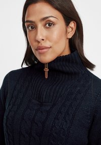 Maglione lavorato a maglia navy con colletto alto a coste e modelli a trecce; presenta una mezza zip con un dettaglio in pelle sul tirante.