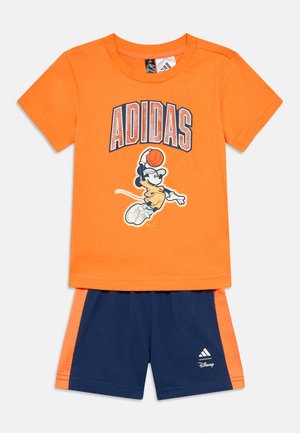 Παιδικό πορτοκαλί μπλουζάκι Adidas με σχεδίαση Mickey Mouse που παίζει μπάσκετ, σε συνδυασμό με σκούρο μπλε σορτσάκι με πορτοκαλί ρίγες στα πλαϊνά.