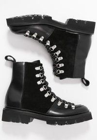 Czarne botki za kostkę z połączeniem zamszu i gładkiej skóry, metalowe haki oraz gruba, teksturowana gumowa podeszwa zapewniająca przyczepność.