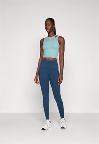 Light blue cropped athletic top with strap details, paired with dark blue leggings featuring a high waistband and side pockets. White sneakers.