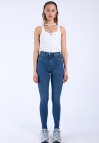 Höga blå jeans med smal passform, tillverkade av denim. Matchat med en vit ribbad tanktop och grå sneakers. Enkla silver smycken.