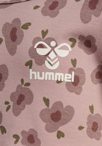 Rosa Textil mit einem Blumenmuster, das dunkelpinke Blumen und grüne Blätter zeigt. Ein weißes Logo mit dem Text "hummel" ist zentriert.