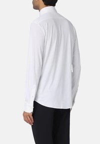 Camicia bianca a maniche lunghe con colletto a punta, polsini con bottoni e vestibilità su misura. Tessuto liscio, nessun motivo e orlo dritto.