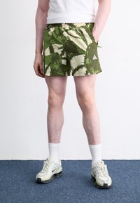 Grønne og beige badeshorts med kaktusmønster, elastisk talje og sidelommer. Båret med hvide sokker og grå sneakers.