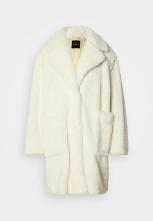 Fehér műszőrme kabát, bemetszett gallérral, nagy elülső zsebekkel és gombos záródással, puha, texturált felülettel és laza fazonnal.
