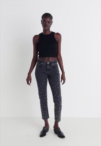Top crop preto sem mangas combinado com jeans cinzentos com detalhes em studs prateados na parte da frente e pernas ajustadas elegantes.