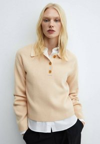 Bleicher Pfirsichfarbener, gerippter Strickpullover mit Kragen, dreiknöpfiger Leiste und langen Ärmeln, übereinander getragen mit einem weißen Hemd. Weiche Textur, lockere Passform.