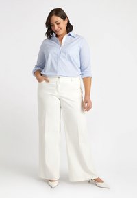 Camicia blu chiaro con colletto bianco; pantaloni a gamba larga color crema; modella che indossa tacchi a punta beige; tessuto morbido.