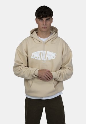 Felpa beige con tasca frontale, caratterizzata da una grafica bianca "CRYSTAL PARIS". Realizzata in tessuto morbido con una vestibilità ampia e cappuccio regolabile.