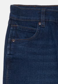 Mörkblå denimjeans med femficksdesign, kontrasterande sömmar och en metallknapp i midjan. Mjuk textur, åtsittande passform.