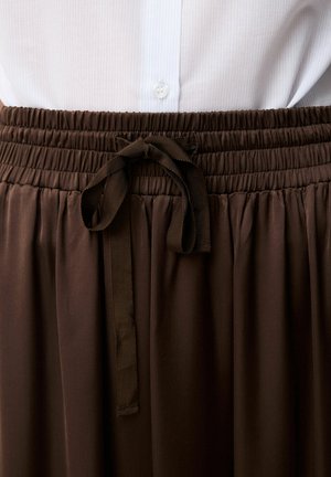 Camisa blanca abotonada metida en una falda marrón de talle alto con cintura fruncida y lazo de cinturón de tela atado en el centro.