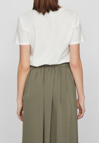 Weißes Baumwoll-T-Shirt mit kurzen Ärmeln, kombiniert mit einem hoch taillierten, gefältelten, olivgrünen Rock, der eine glatte Textur und einen subtilen Fall zeigt.