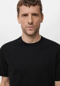 Tricou negru cu mânecă scurtă și guler rotund, confecționat dintr-un material neted. Design ajustat cu cusături minime și o textură ușor ribmedă la guler.