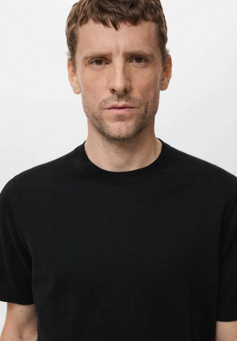 Schwarzes T-Shirt mit kurzen Ärmeln und Rundhalsausschnitt aus glattem Stoff. Enganliegendes Design mit minimalen Nähten und einer leichten Rippstruktur am Kragen.