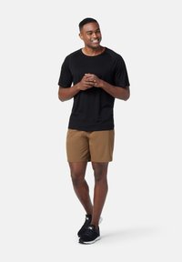 Černé tričko s krátkým rukávem v kombinaci s hnědými šortkami. Model má na sobě černé sportovní boty. Jednoduchý design, hladká tkanina a neutrální barvy.