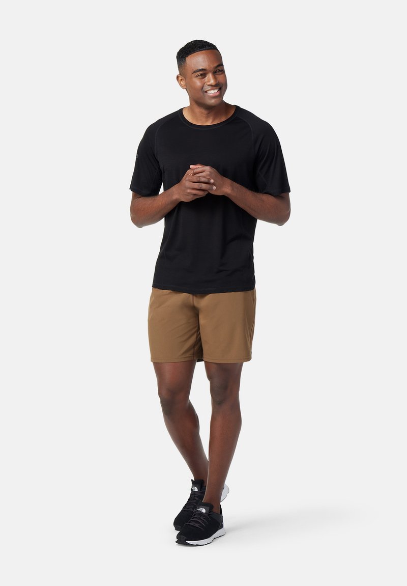 Černé tričko s krátkým rukávem v kombinaci s hnědými šortkami. Model má na sobě černé sportovní boty. Jednoduchý design, hladká tkanina a neutrální barvy.