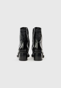 Čierne kožené členkové čižmy s lesklým povrchom, stredne vysokým blokovým podpätkom a bočným zipsom. Hladká textúra s minimálnymi detailmi.