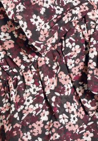 Tissu noir avec de petits motifs floraux blancs, roses et rouge foncé, comprenant des parties plissées et repliées créant de la texture.