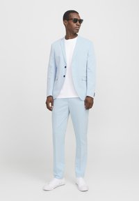 Svetlo modro suknjo s slim fit krojem, enovratnim blejzerjem in usklajenimi hlačami. Belo majico in bele superge dopolnjujejo obleko.