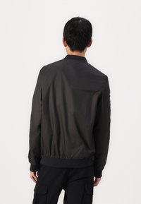 Black bomber jacket with elastic cuffs and hem, smooth material, and a stand collar. Simple design with no visible patterns or hardware details.