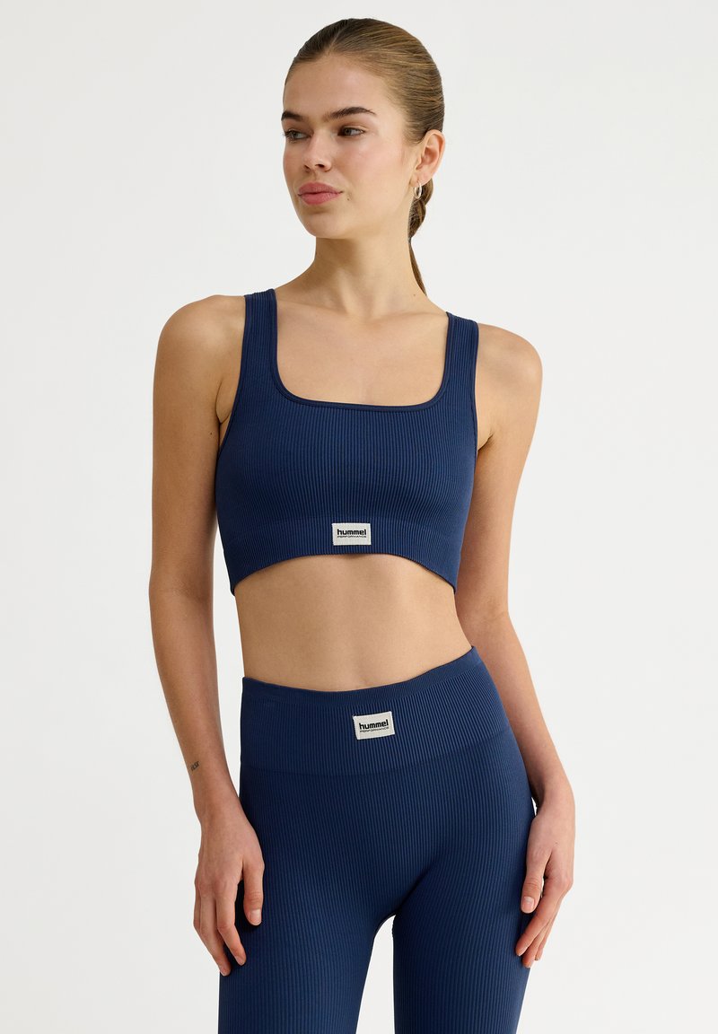 Marinblå ribbad croptopp med fyrkantig halsringning, kombinerad med högmidjade leggings med ett varumärkestygmärke på midjebandet. Mjuk textur.