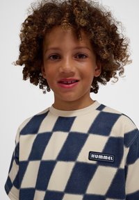 Kortärmad skjorta med en krämfärgad bas och ett mörkblått rutmönster. Har en "HUMMEL" logopol på framsidan. Mjuk textur.