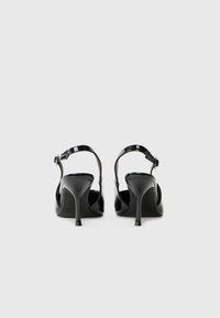 Sorte patent lær højhælede sandaler med en slank rem og justerbar ankelspænde, med spids tå og stiletto hæl.