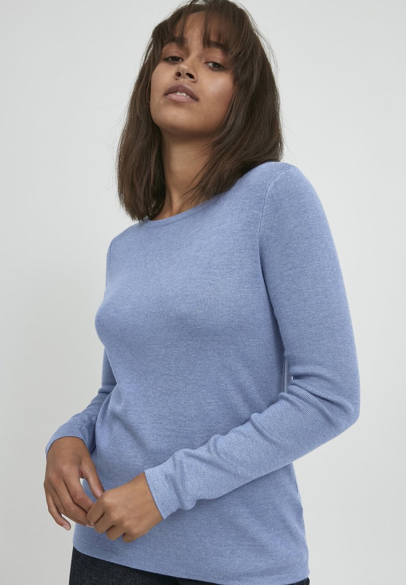 Svetlo modra dolgosleeve pulover s okroglim izrezom, rebrasto teksturo in prilegajočim oblikovanjem. Tkanina se zdi mehka in elastična.