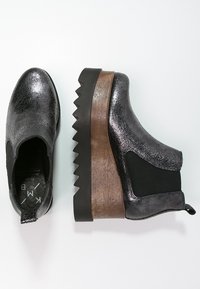 Mustat metallivuoratut nilkkasaappaat, joissa on teksturoitu pinta, joustavat sivupaneelit ja tukeva, sahalaitainen pohja, jossa on puinen yksityiskohta kantapäässä.