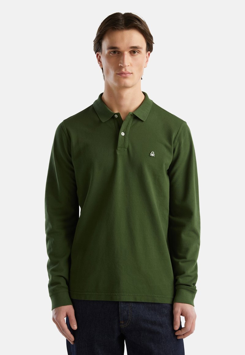 Zielona polo z długimi rękawami, z bawełnianej tkaniny, z zapięciem na guziki i małym logo na lewej piersi. Noszona z ciemnymi dżinsami.