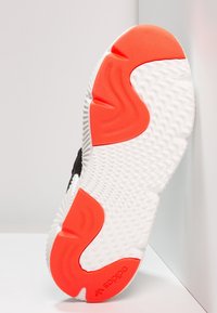 Svart och vit atletisk skon sula har en texturerad yta, en ljus orange accent och en framträdande Adidas-logga på hälen.