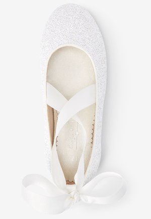 Ballerine blanche pailletée avec des brides en ruban croisées nouées en nœud, vue de dessus sur fond blanc.