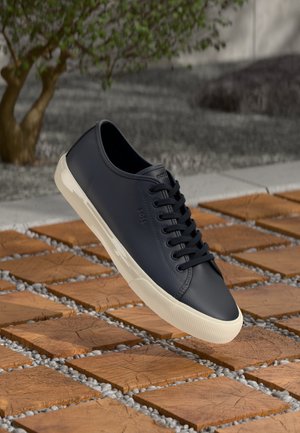 Navy leather sneaker with a low profile, round toe, and rubber sole. Features a textured upper and laces, displayed above a tiled surface.