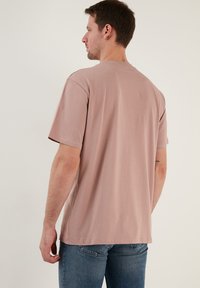 Ljust rosa bomulls T-shirt med rund halsringning och kort Ärmar, visad bakifrån, med en slät textur och avslappnad passform.