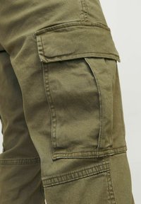 Κοντινό πλάνο τσέπης χακί cargo παντελονιού με καπάκι και ορατή ραφή στο ύφασμα.