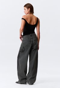 Μαύρο τοπ με ανοικτούς ώμους, συνδυασμένο με χαλαρά, σκούρα γκρι τζιν τζιν με πίσω τσέπη και διακριτικές ραφές.