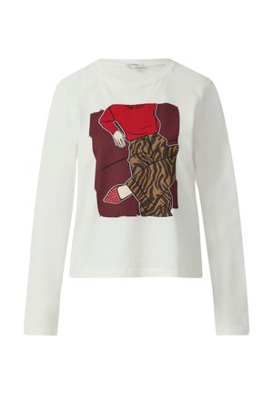 Witte t-shirt met lange mouwen, voorzien van een rood grafisch ontwerp van een zittende figuur, gecombineerd met bruine met patroon versierde broek en rode schoenen met stippen.