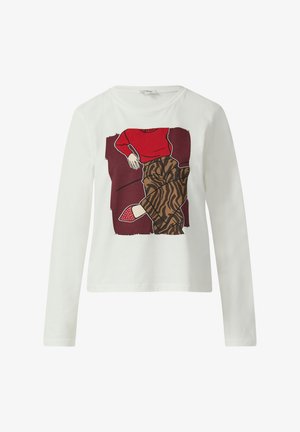 Biała koszulka z długim rękawem z czerwoną grafiką przedstawiającą siedzącą postać, zestawiona z brązowymi spodniami w wzory oraz czerwonymi butami w kropki.