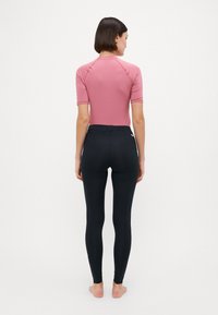 Maglietta a manica corta rosa abbinata a leggings neri a vita alta, progettata per un look aderente, con una texture liscia e dettagli minimali.