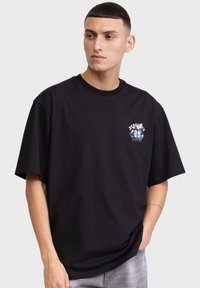Schwarzes, übergroßes Baumwoll-T-Shirt mit einem bunten Grafikdesign auf der Brust. Rundhalsausschnitt, kurze Ärmel und lockerer Schnitt.