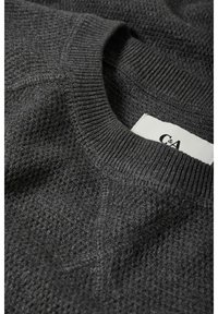 Pull en maille gris foncé avec col rond côtelé et motif texturé subtil, étiquette de vêtement partiellement visible à l'intérieur du col.