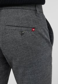 Gray plaid trousers made of a textured fabric, featuring a side pocket with a dark button and a small red tag on the pocket edge.