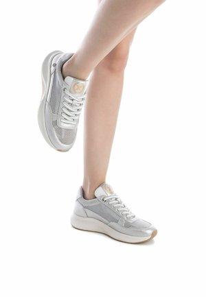 Zapatilla blanca con tejido de malla, punta redonda, cuello acolchado y acentos en color beige. Presenta una suela texturizada y un diseño de cordones.