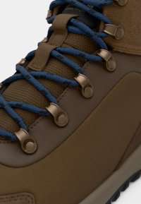 Brown hiking boot featuring textured synthetic material, blue laces, metal eyelets, and a cushioned collar for enhanced support.